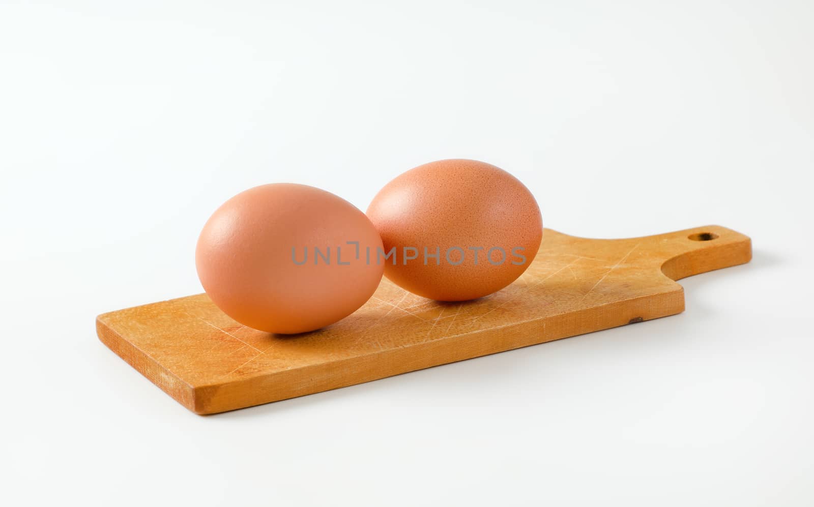 Two brown eggs on wooden cutting board