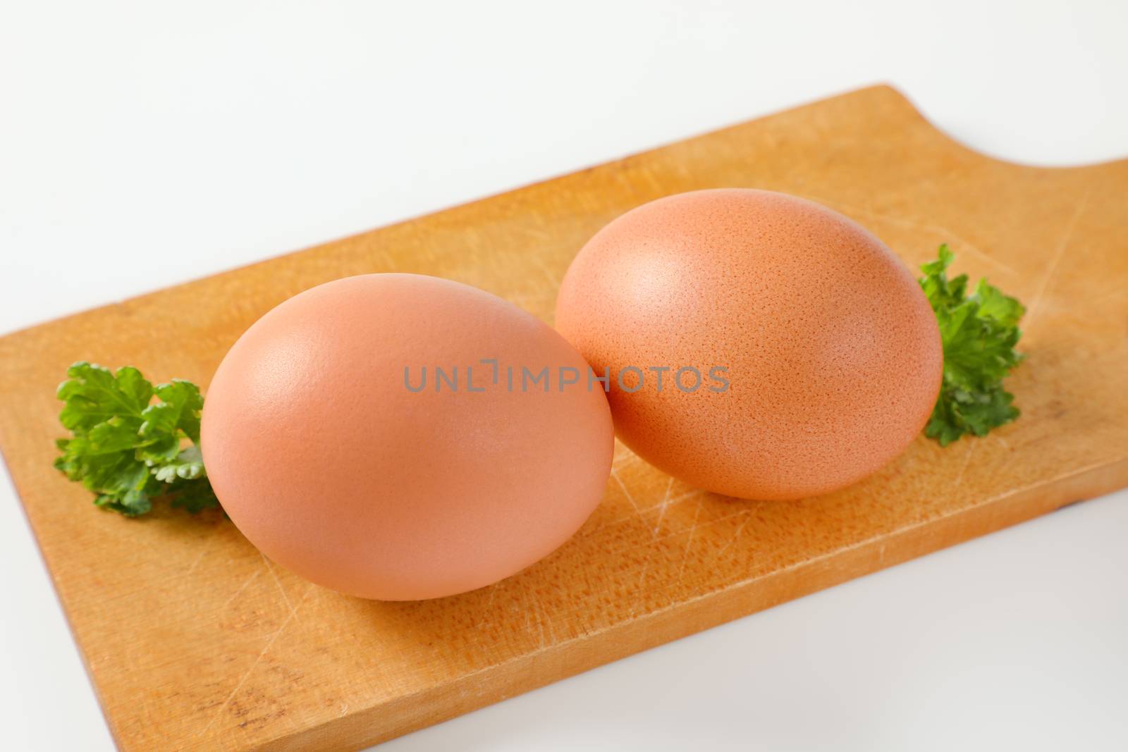 Two brown eggs on wooden cutting board