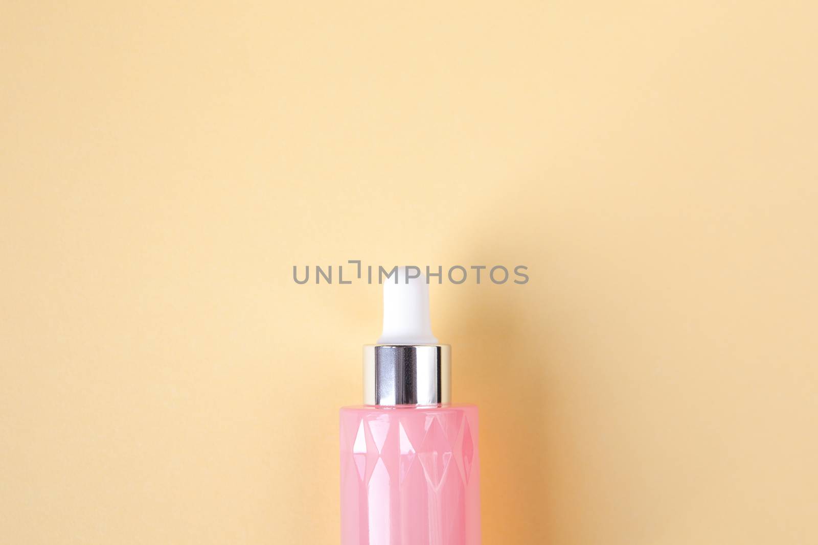 Pink glass bottle with beauty serum for face on pastel yellow background, copy space. Top view. Concept beauty rituals, homemade cosmetic, skin care. Minimal style, place for text. Horizontal.