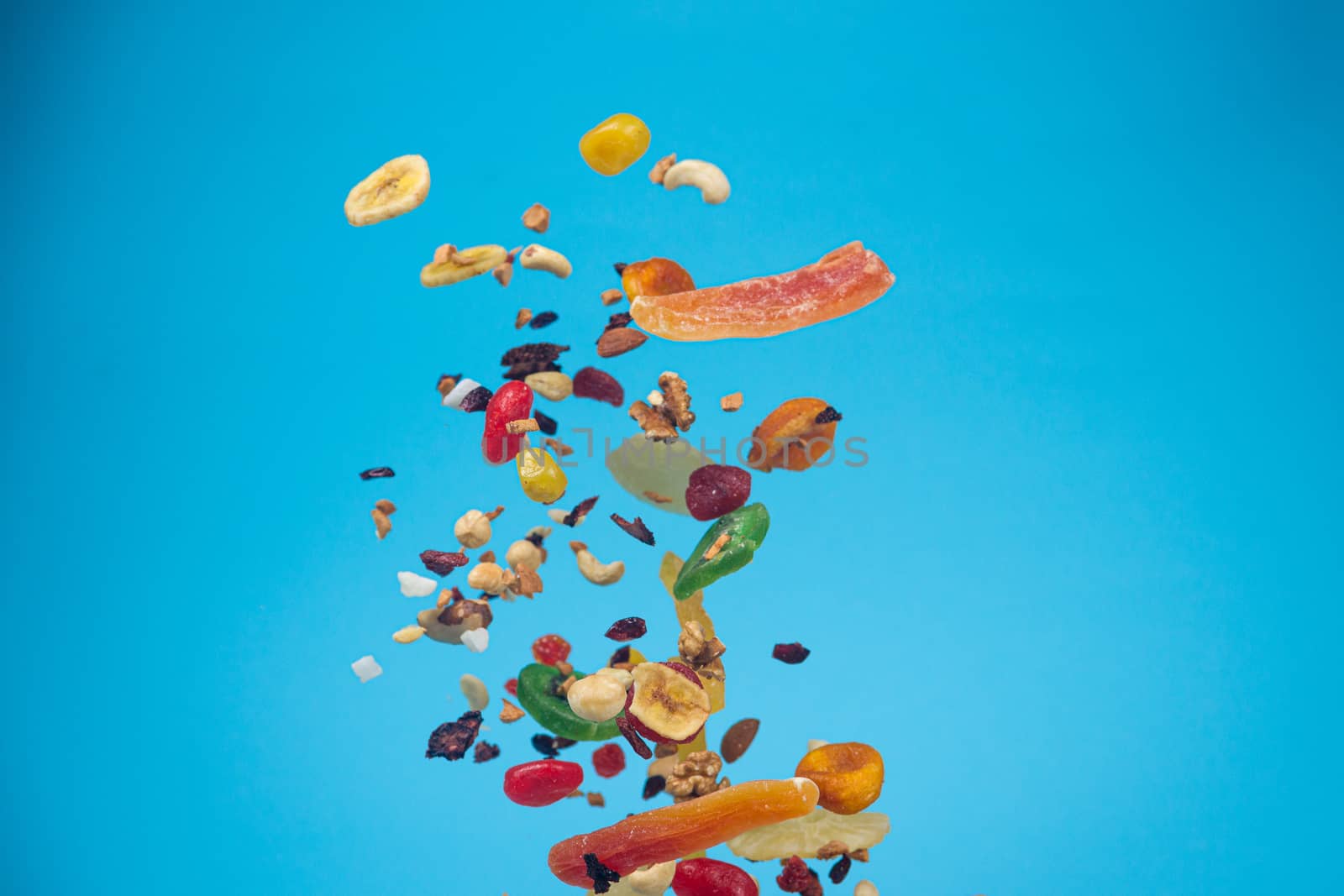 Dried and candied fruits and nuts flying on blue background. Stock photo of healty and nutrient food. Conceptual photo of vegan and vegetarian healty food.