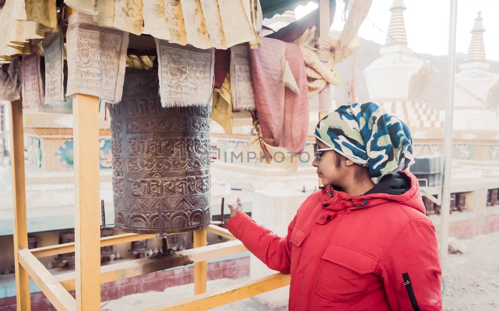 A solo traveler Indian woman in warm clothing turning Buddhist prayer wheel drum of a Buddhist monastery. Travel Holiday vacation background. Kaza, Himachal Pradesh, India, South Asia May 2019 by sudiptabhowmick