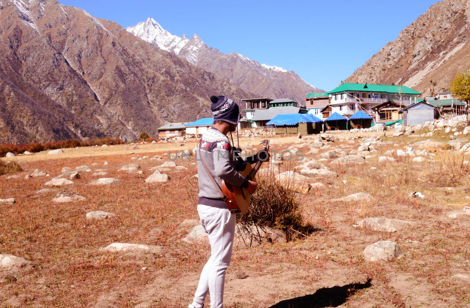 A solo traveler hobbyist musician playing guitar alone in the silence of Himalayan mountain valley and sound of guitar strings. Summer music Inspiring environment in outdoors. Sangla India South Asia. by sudiptabhowmick