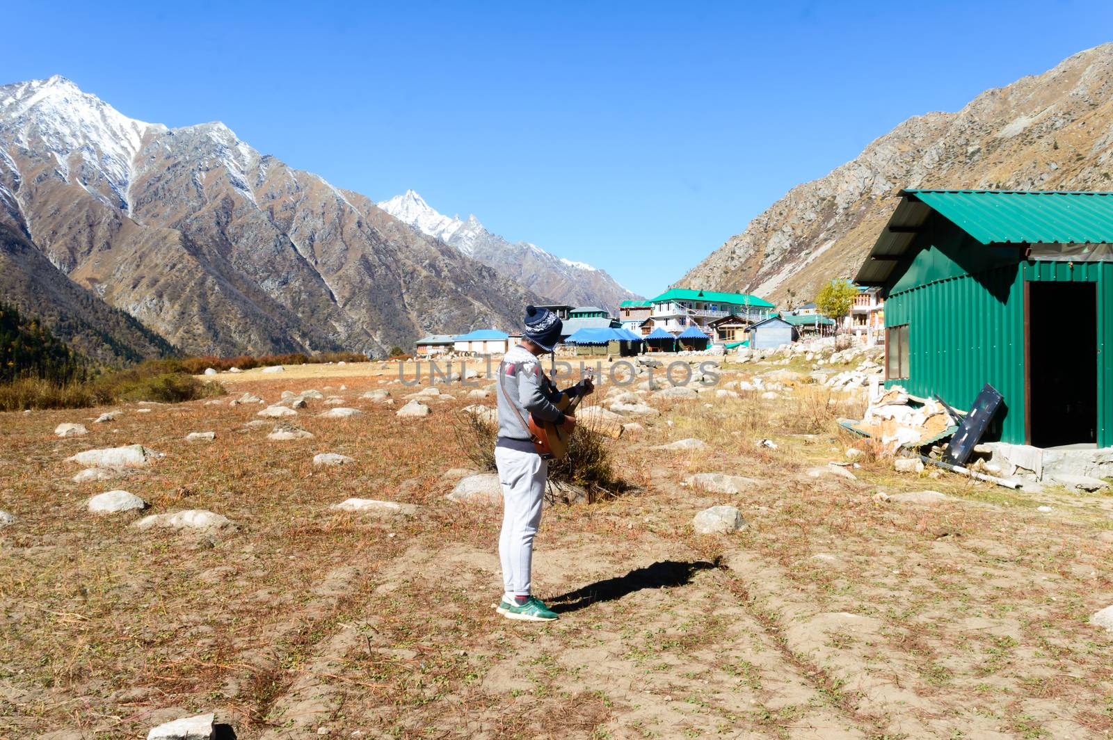 A solo traveler hobbyist musician playing guitar alone in the silence of Himalayan mountain valley and sound of guitar strings. Summer music Inspiring environment in outdoors. Sangla India South Asia.