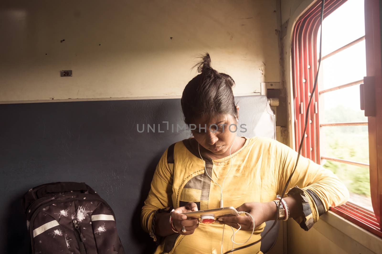 Woman using mobile phone while traveling solo in passenger train. Traveler enjoying Modern technology on the move in everyday life and travel. Close up portrait - Young Adult Lady - Indian ethnicity. by sudiptabhowmick