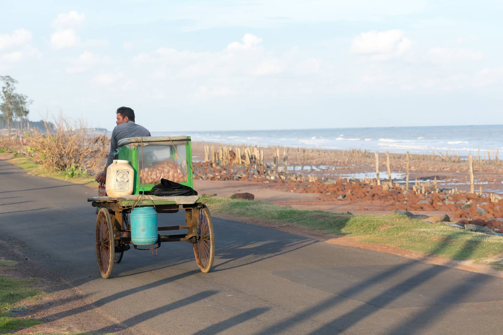 A rural local village mobile street food seller selling phuchka, gol gappa, chaat and pani puri on traditional cycle rickshaw van vehicle in coastal area beach road in summer sunset. India, May 2019