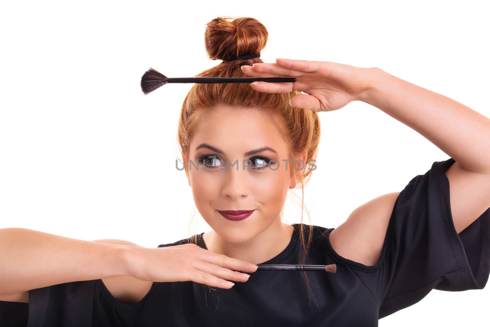 Beautiful young girl with perfect skin framing her face with cosmetic brushes for make-up, smiling and looking to the side, isolated on white background.