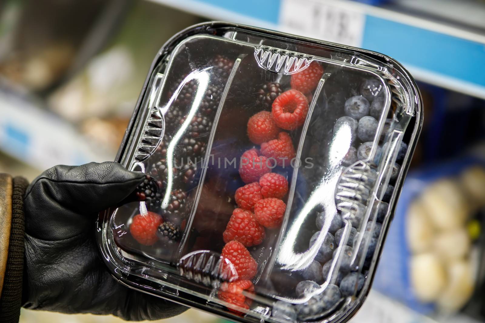 A man's hand holds a plastic box of berries in a grocery store. Plastic product packaging.