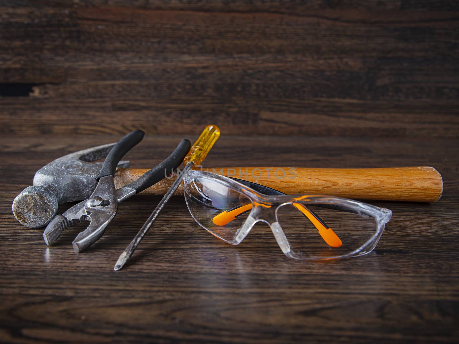 hammer, pliers, flat screw driver and protection glasses on a hard wood floor background
