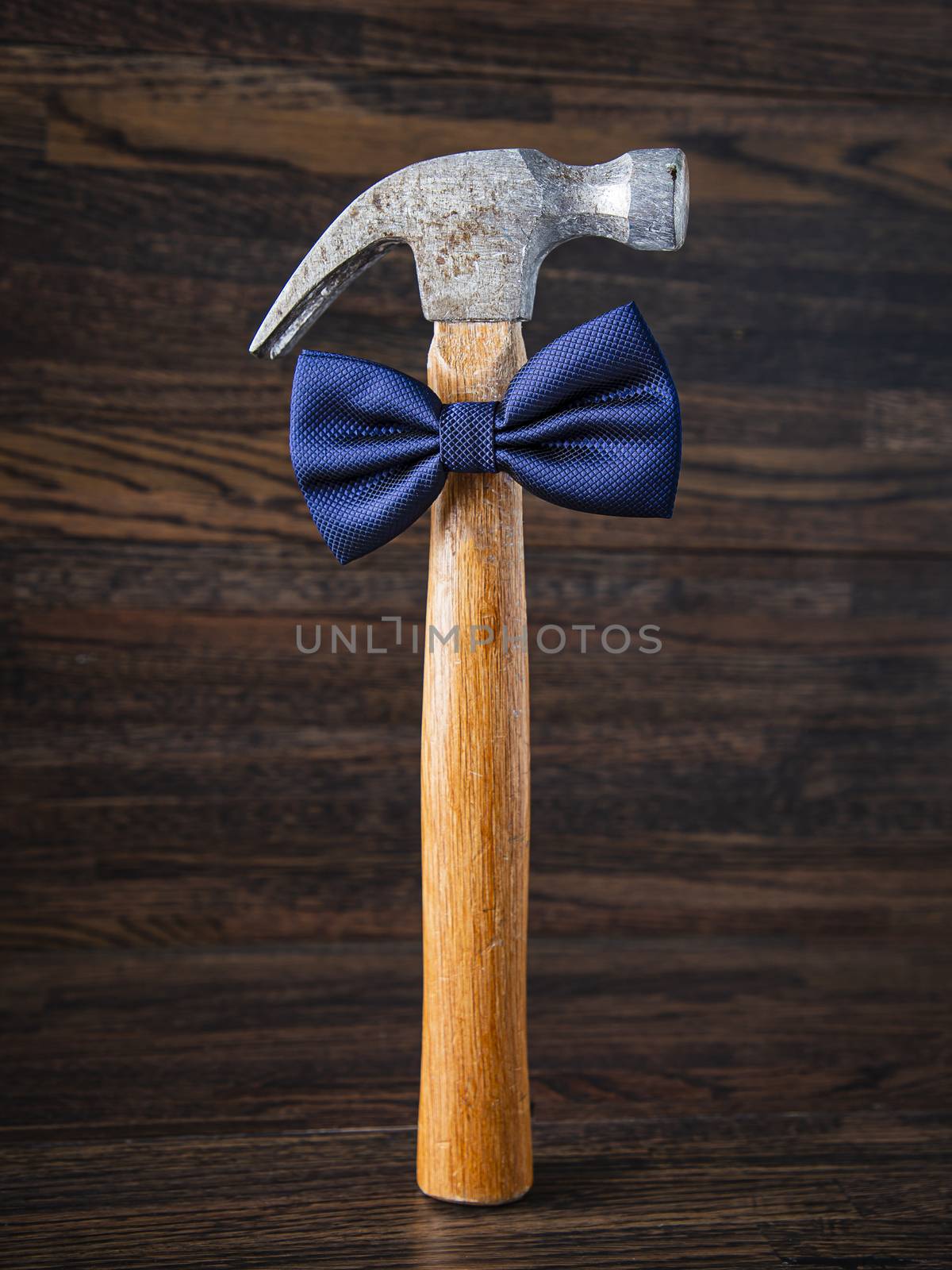 weathered down hammer wearing a blue bow tie against a hard wood floor backgound