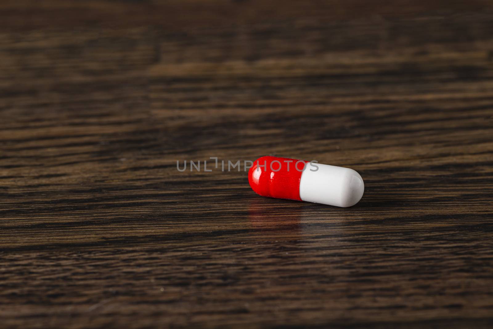 close-up of a red and white pill against a dark wood background