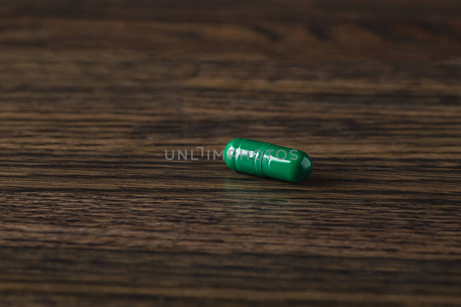 close-up of a green pill against a dark wood background