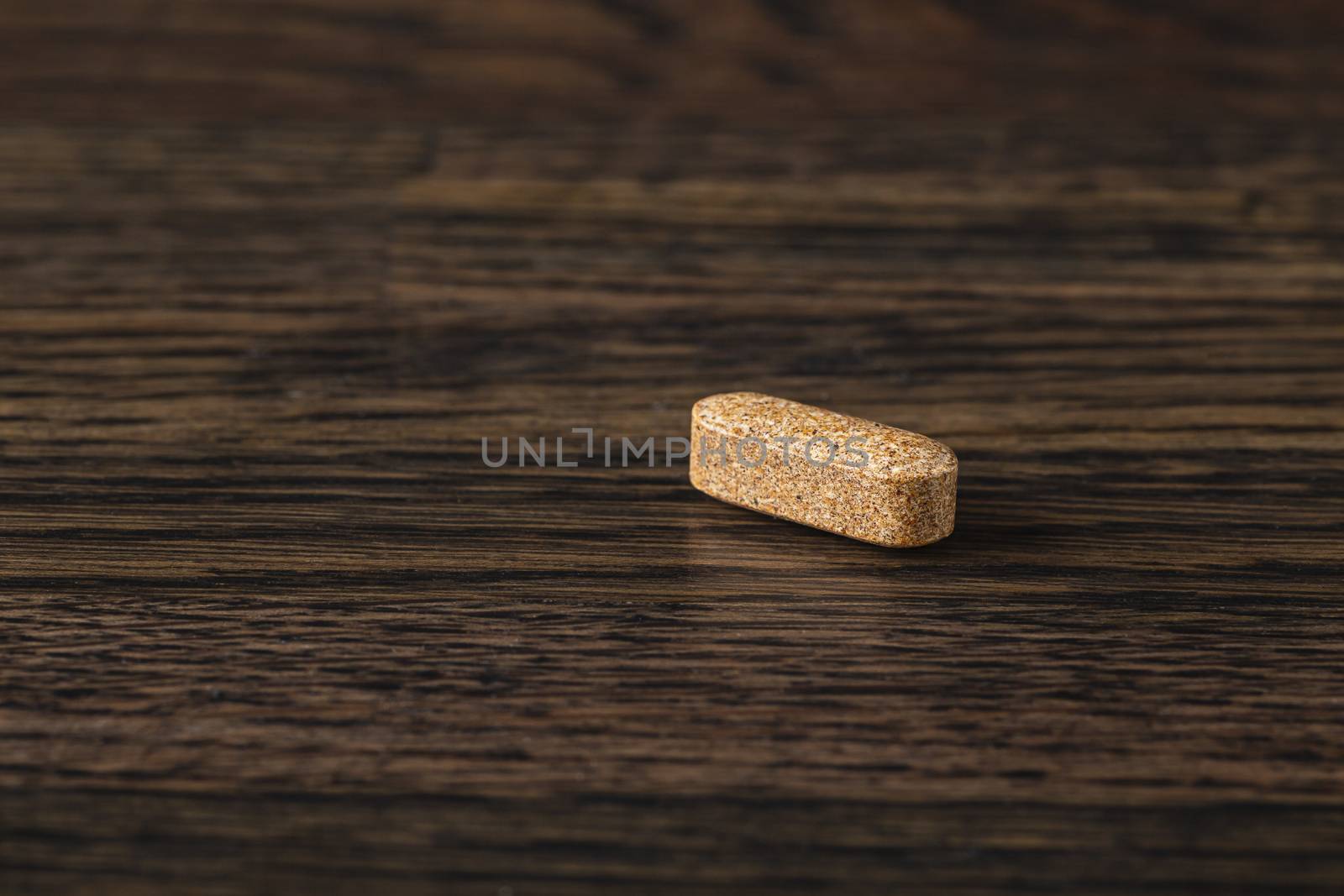 close-up of a brown natural supplement tablet against a dark wood background