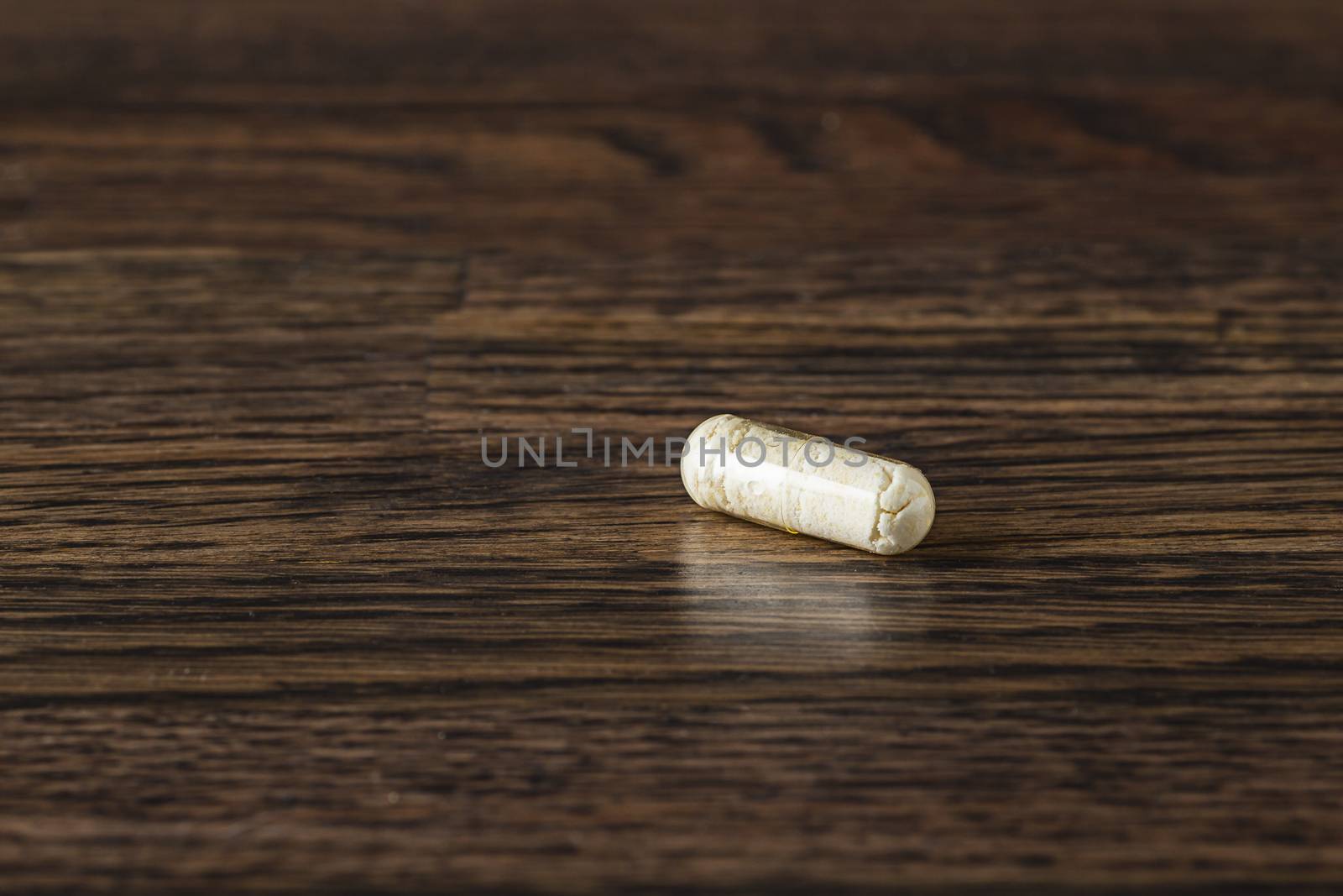 close-up of a transparent pill packed with white ingredient against a dark wood background