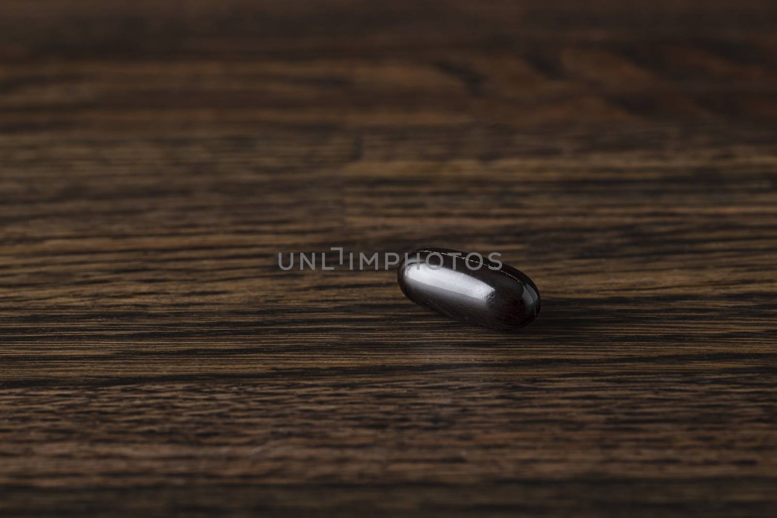 close-up of a large black omega 3 pill against a dark wood background