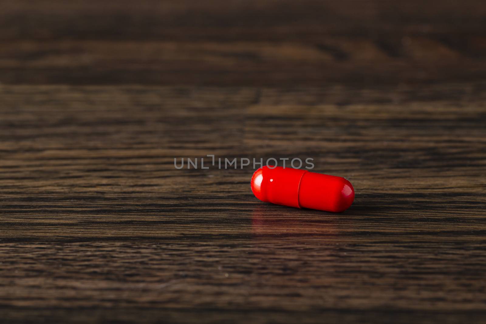 close-up of a red pill against a dark wood background