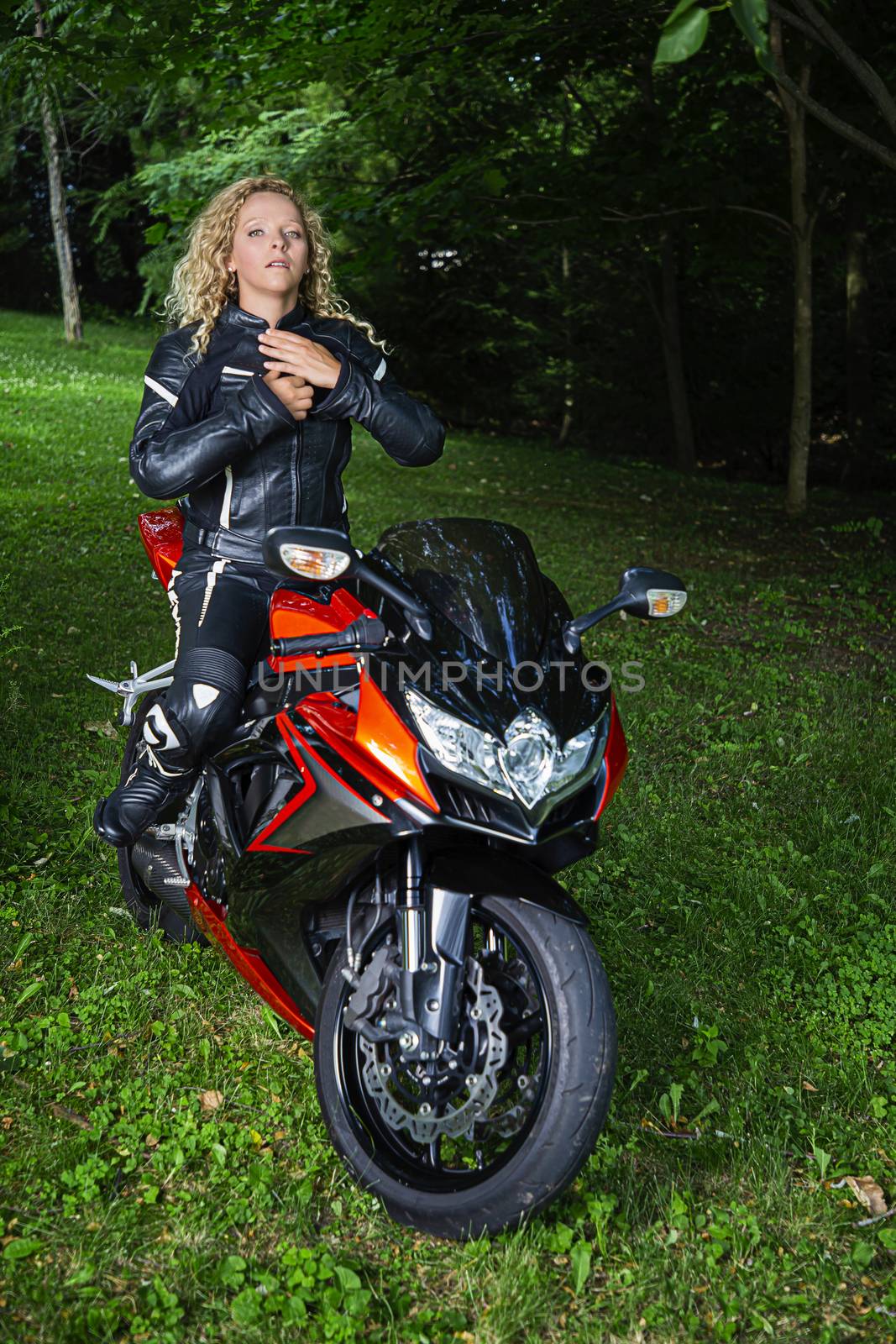 young blond motocyclist zipping up her leather jacket while sitting on her sport motocycle