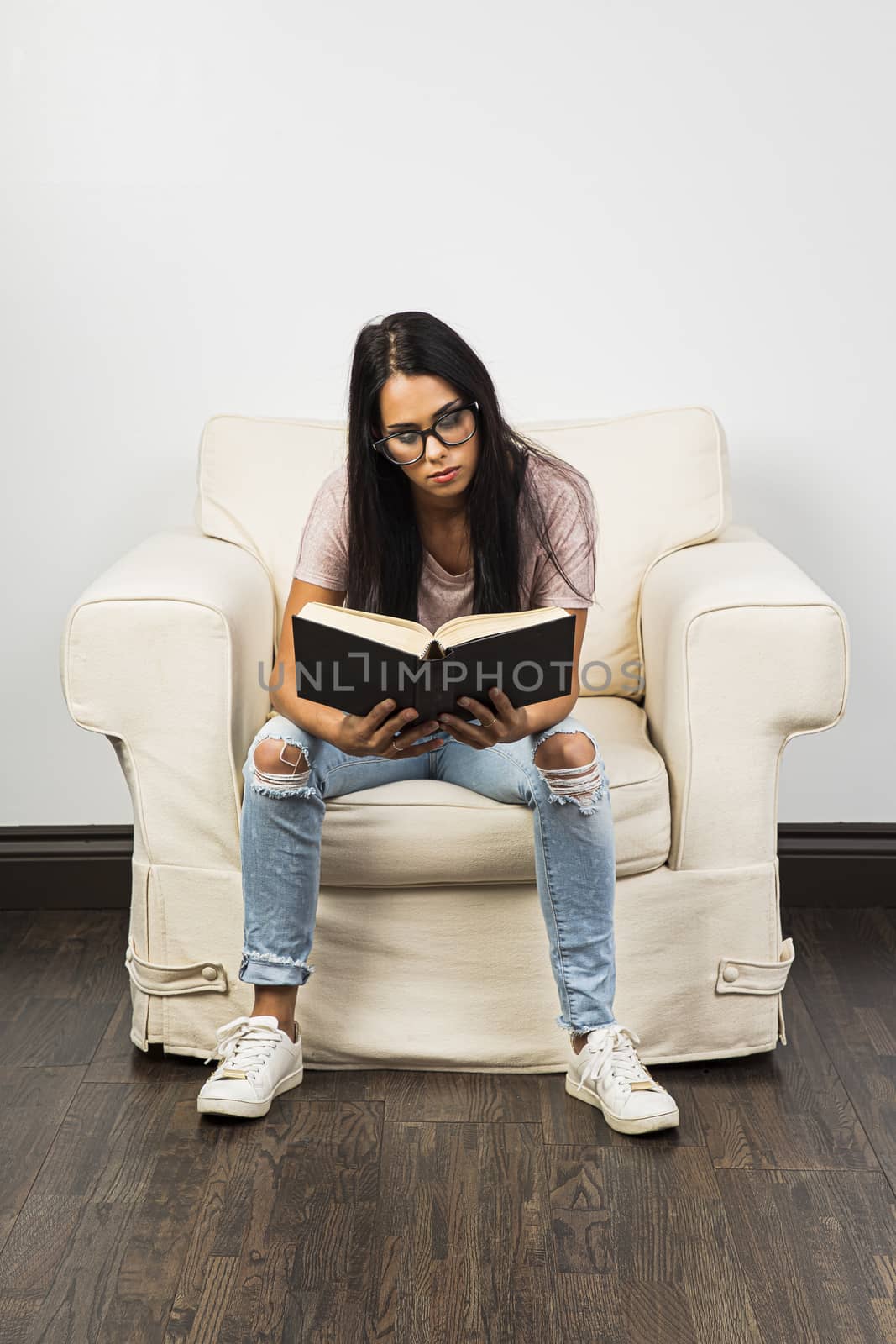Twenty something woman wearing glasses, sitting on a couch, reading a hard cover book