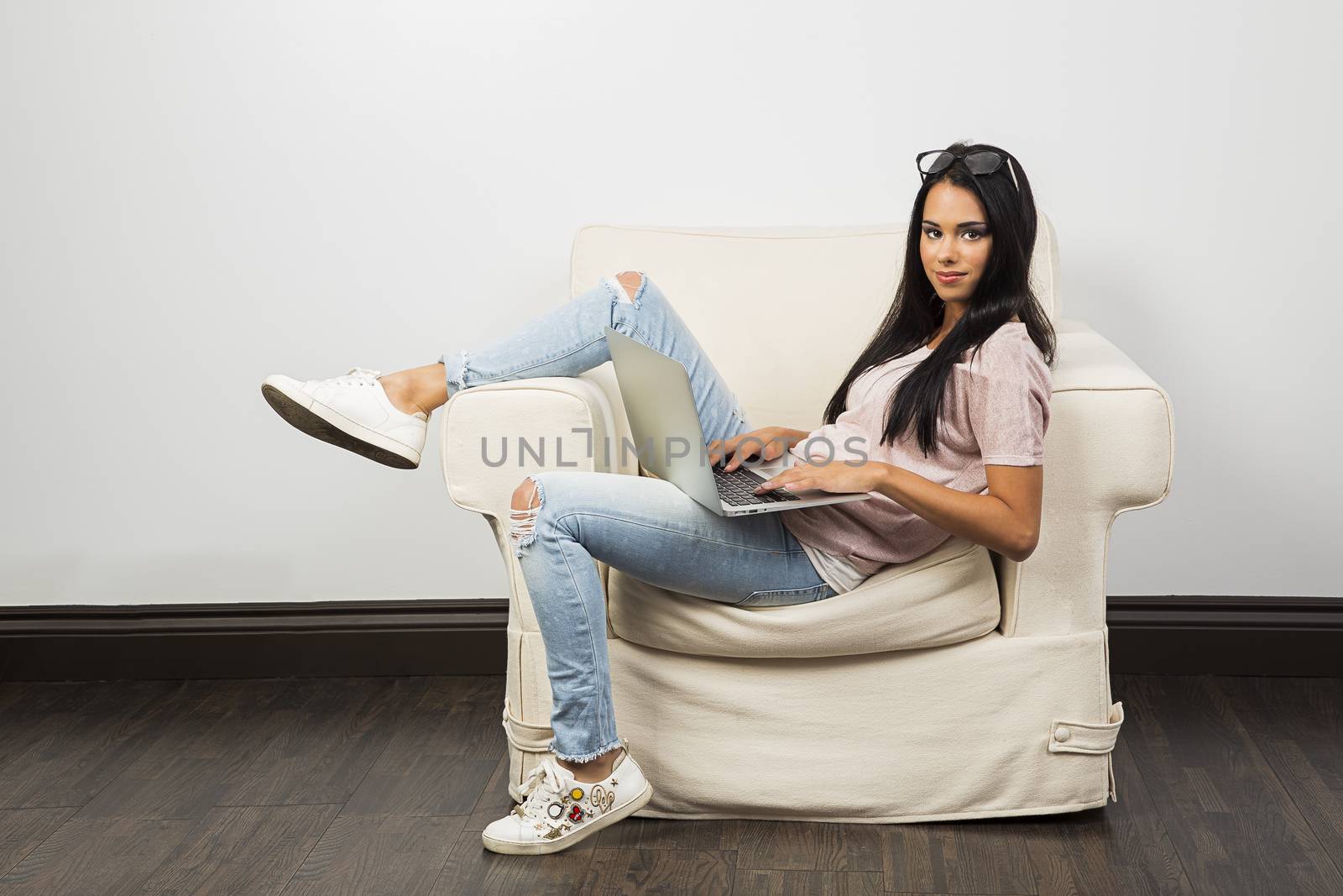 young woman, with her leg up on the arm of a couch, working on a laptop