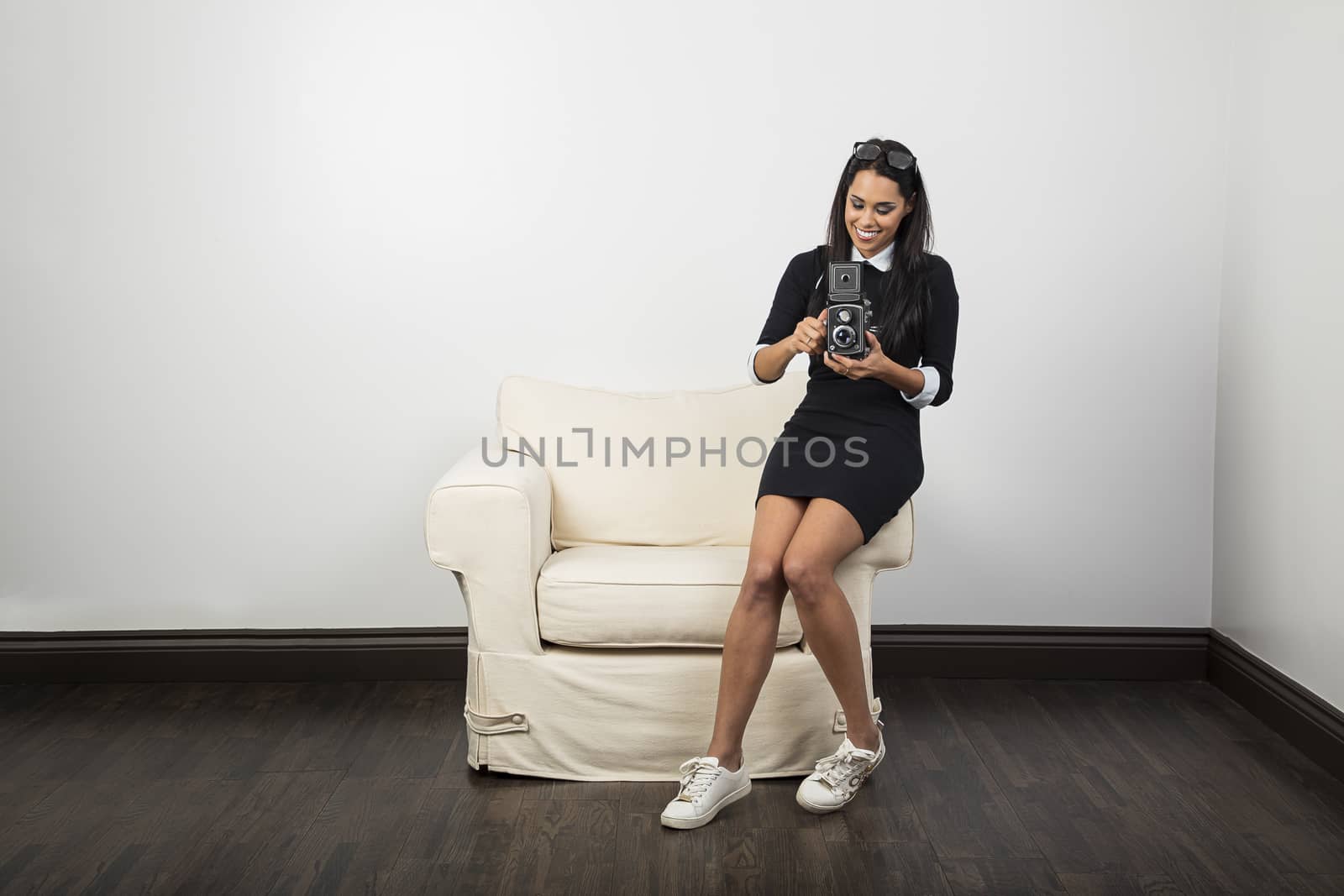 Millenial girl sitting on a white couch using a vintage camera