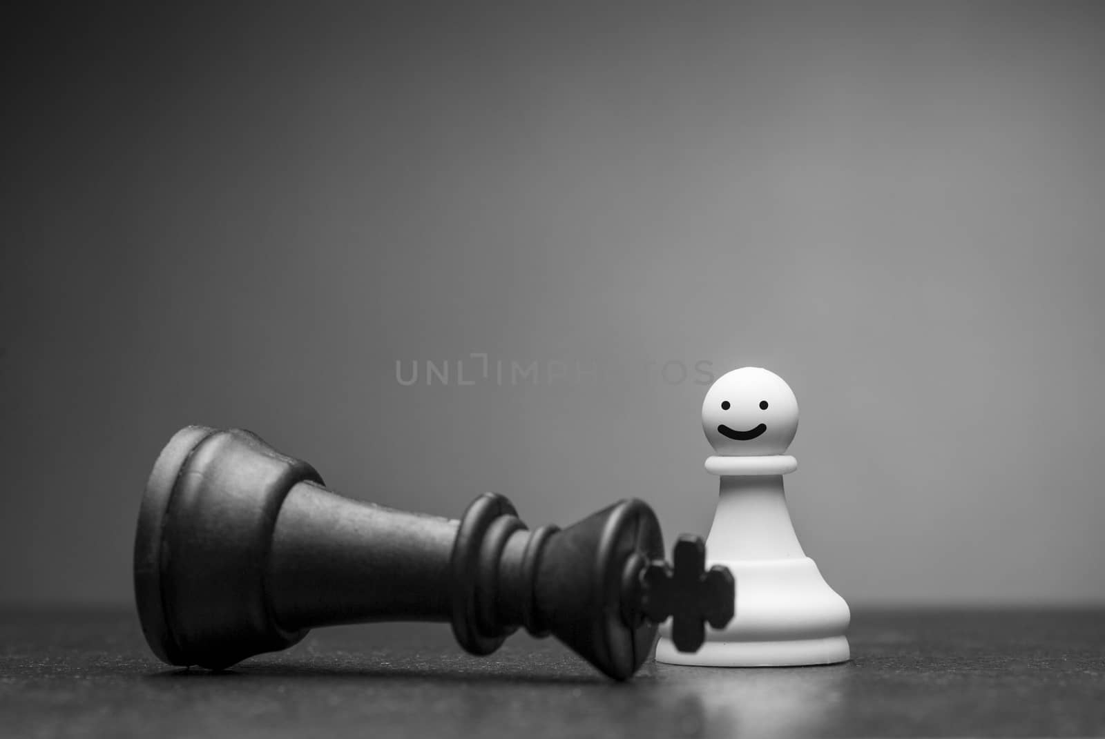 White pawn chess piece smiling at a fallen black king over a grey background with copy space in a conceptual image