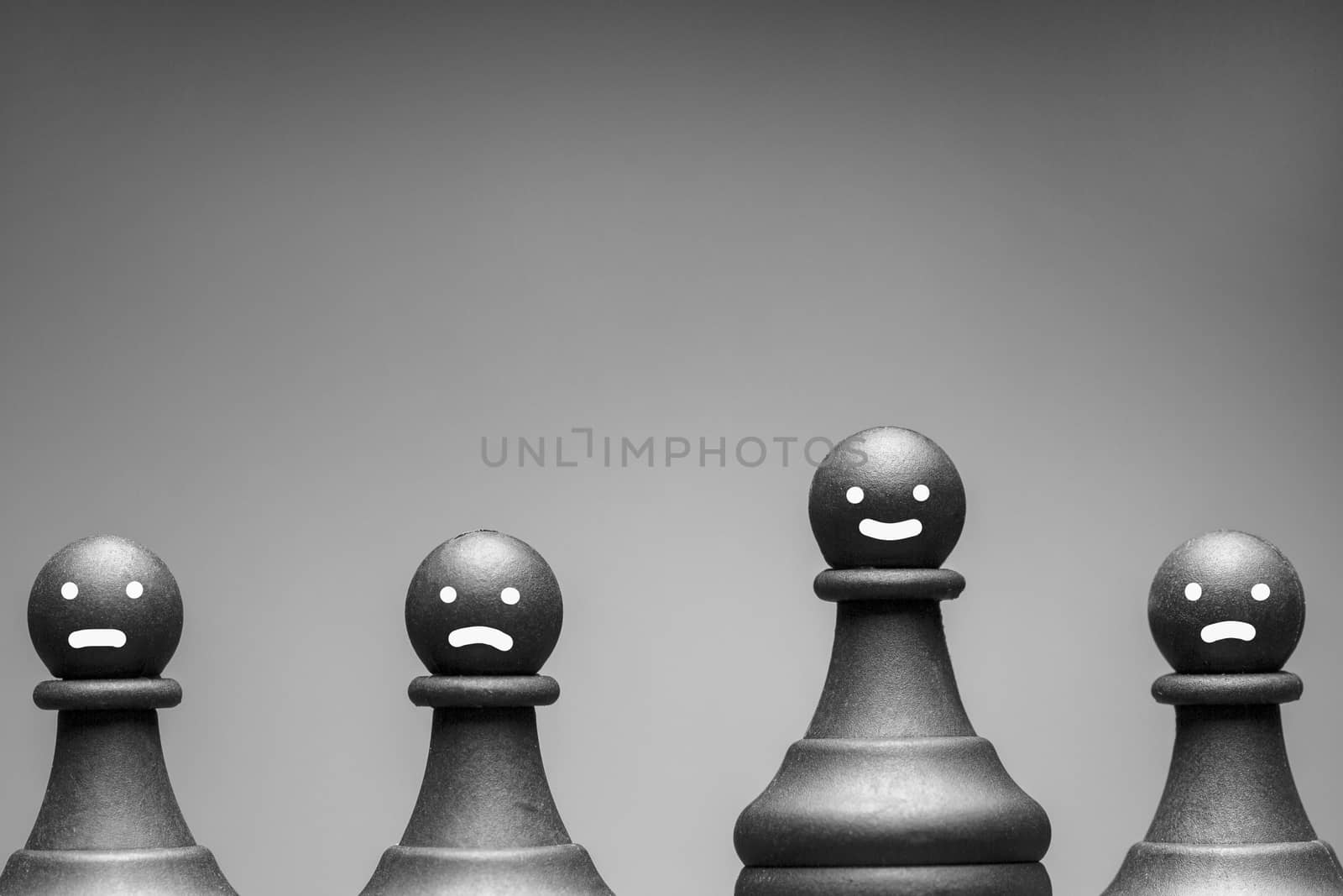 Greyscale image of chess pieces with faces showing happy, neutral and cross expressions on pawns with copy space above
