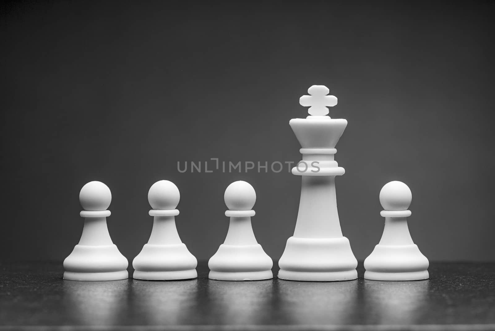 White king chess piece with row of pawns over a grey background with copy space on a reflective surface