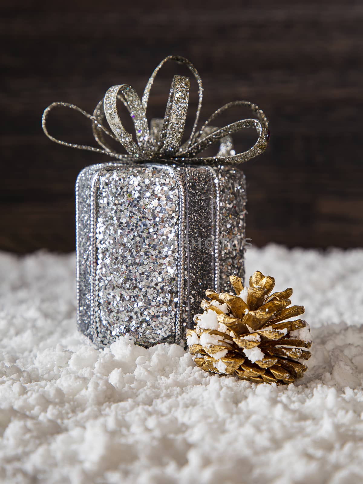 silver wrap present and golden pine cone in the snow against a wood background