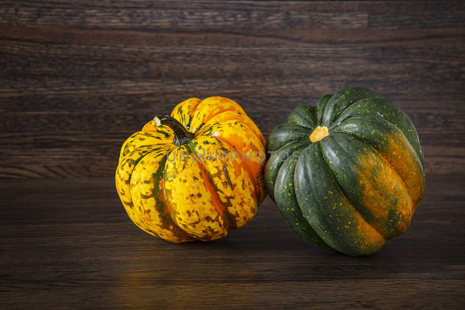 two Sweet Dumpling squash, one orange, one green against a wood background