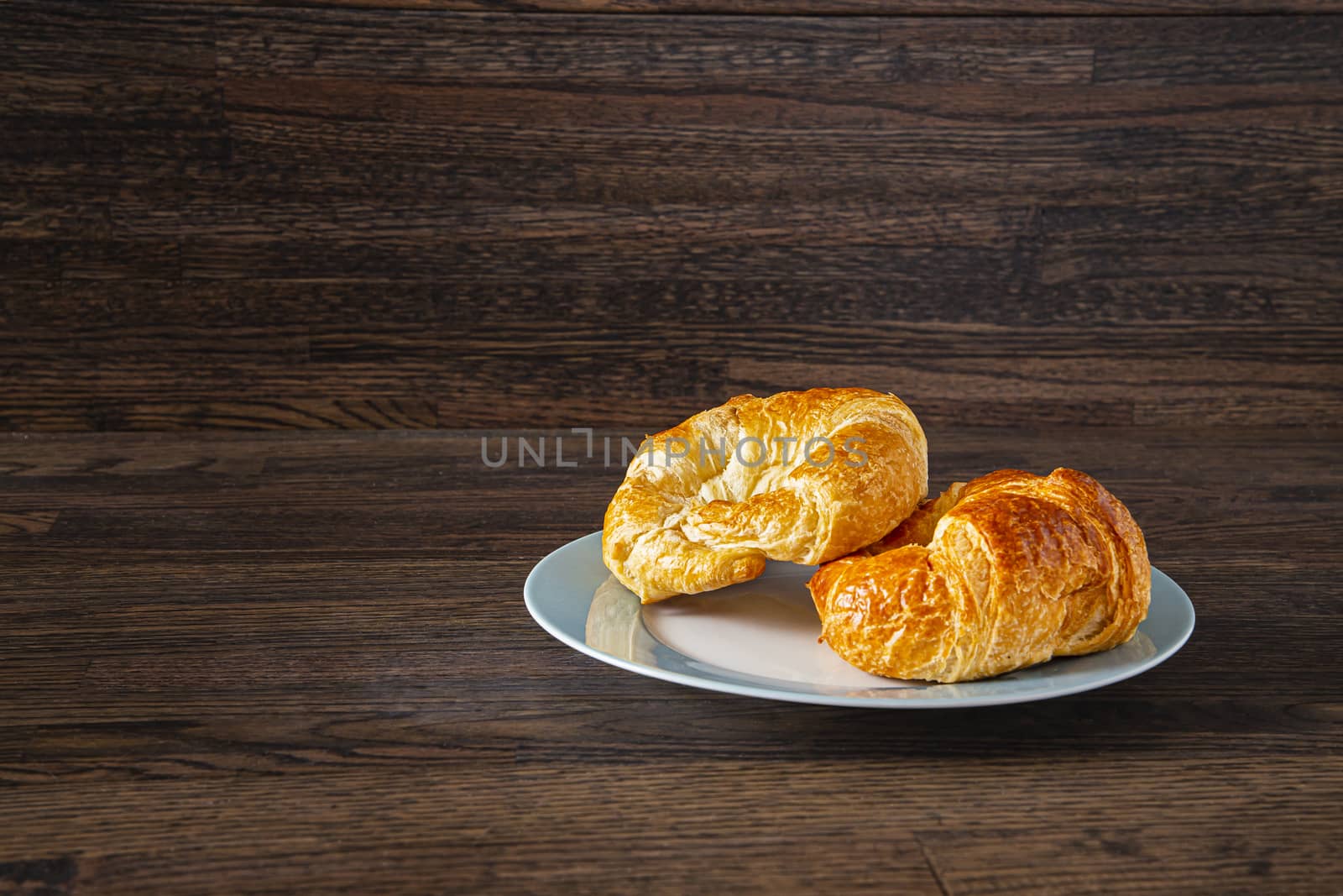 two croissant on a blue rim plate on a dark wood background