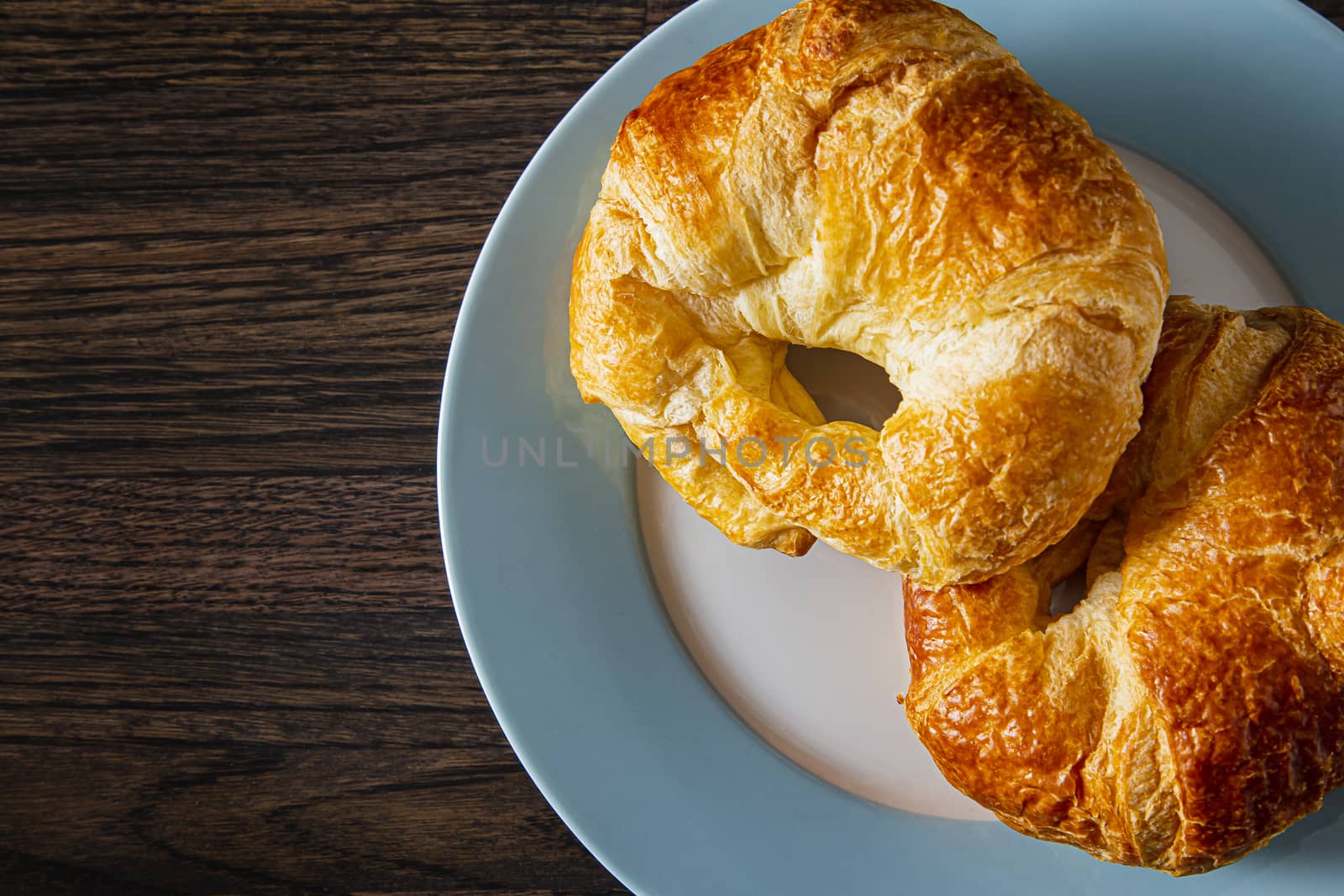 top view of two croissants on a blue rimmed plate against a dark brown wood background