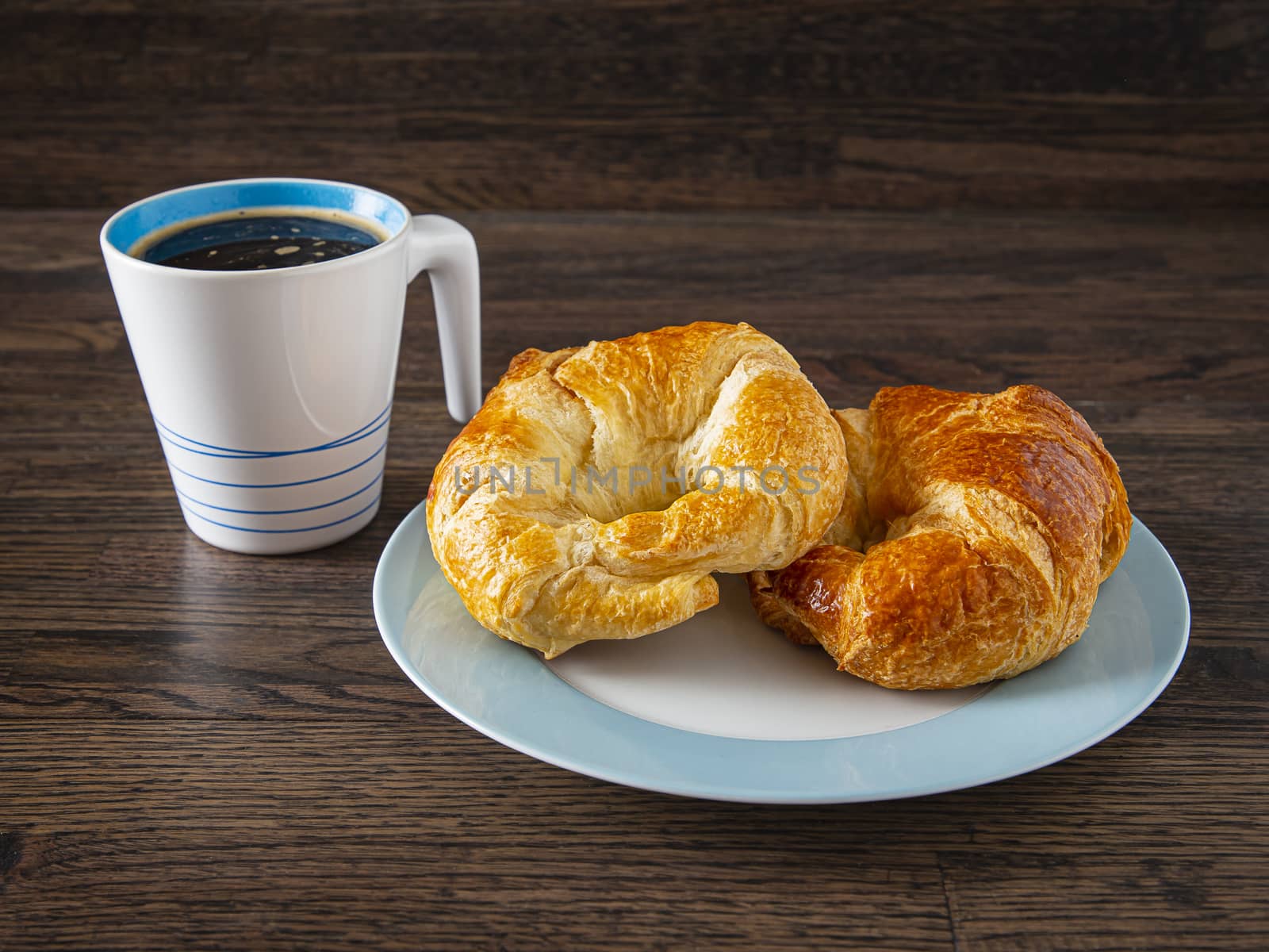 cup of coffee and two croissant on a plate against a dark brown wood background