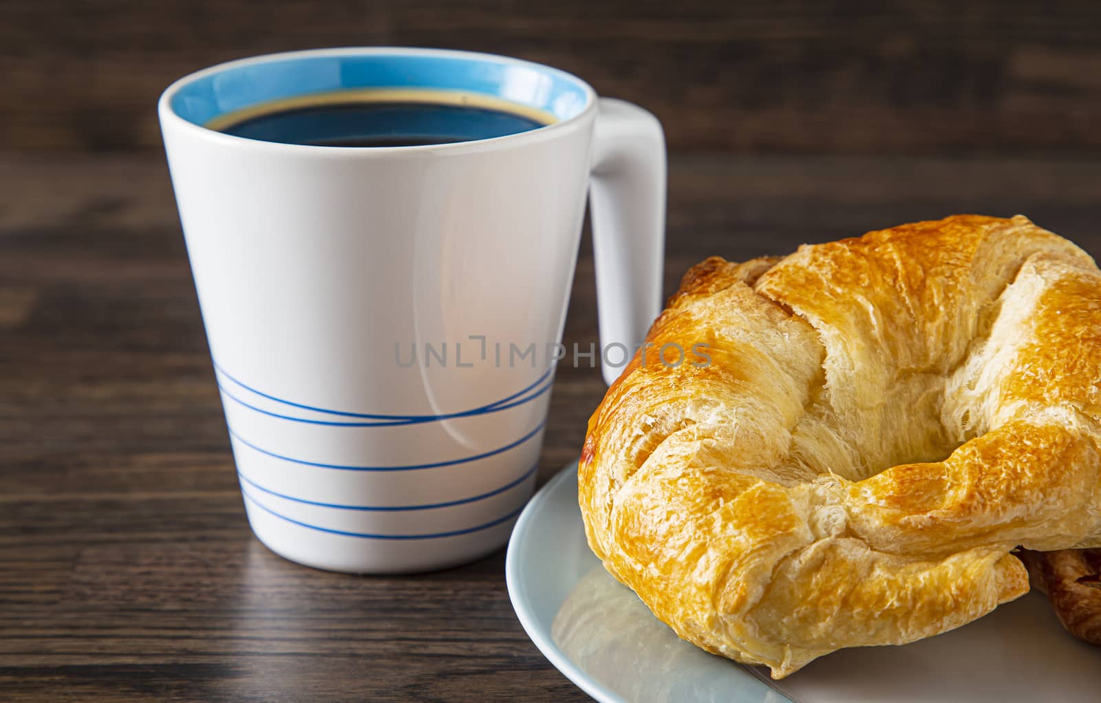 cup of coffee and croissant against a dark brown wood background