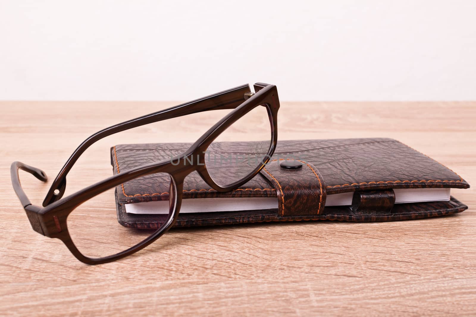 Close up of a planner notebook and glasses placed on a wooden table.