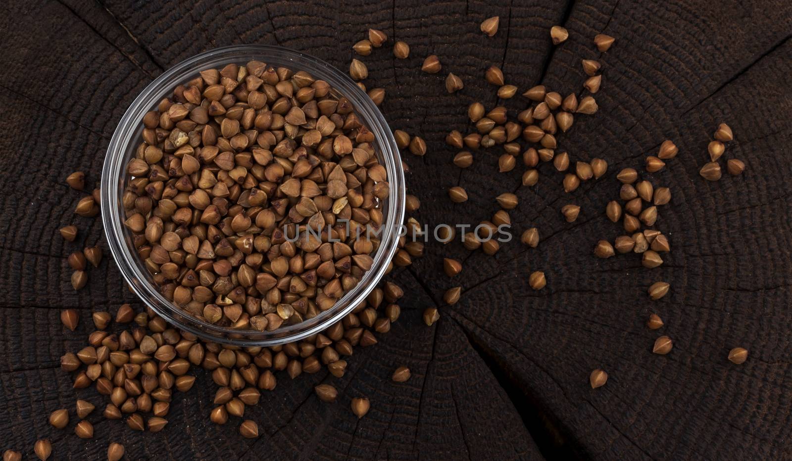Bowl of buckwheat grains on black wooden background, top view