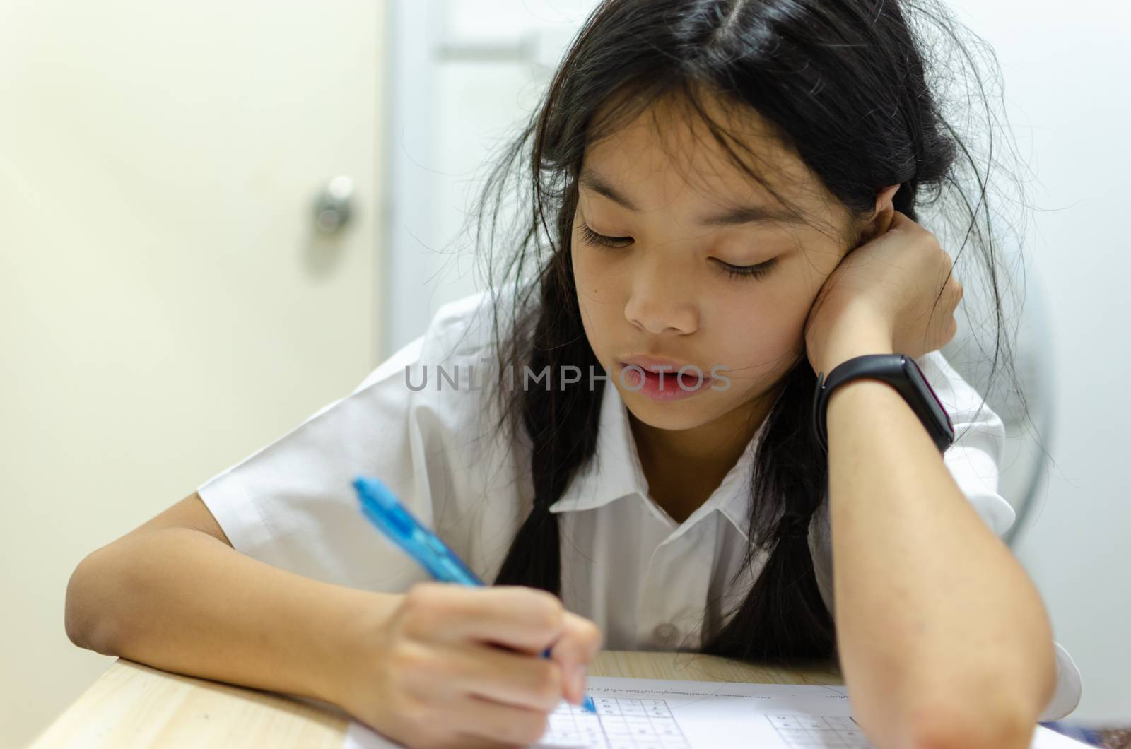 Beautiful young Asian girl wearing a school uniform was intended homework at the table.