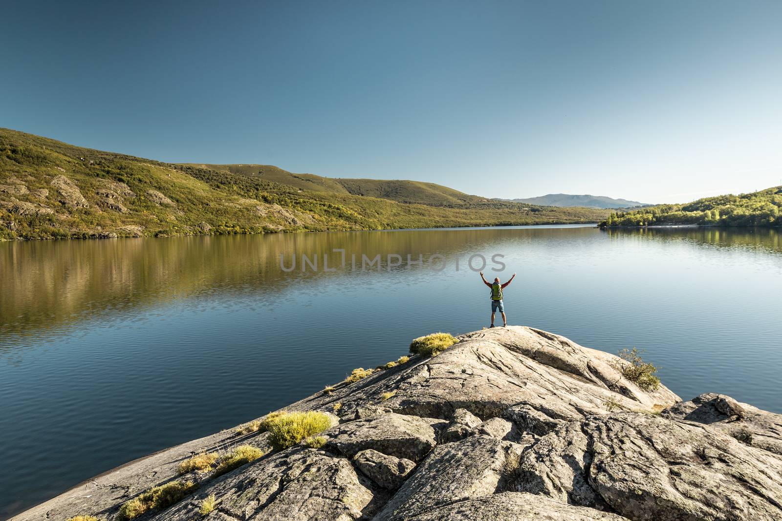 Shot of a man hiking near a beautiful lake with arsm raised