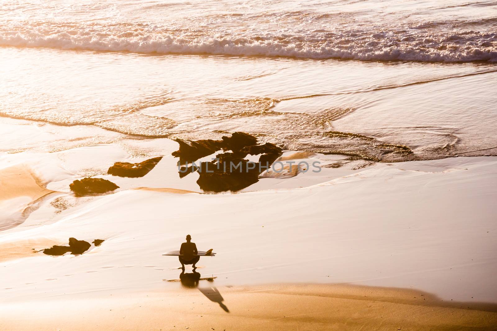 Top view of a surfer sitting 
on the beach