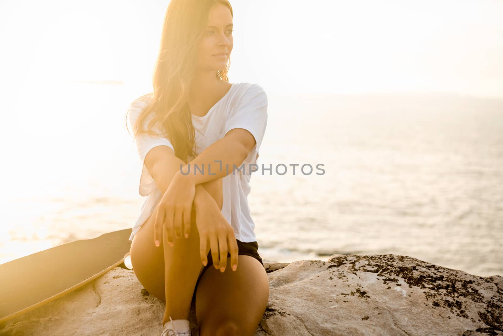 Beautiful and fashion young woman posing at the sunset with a skateboard