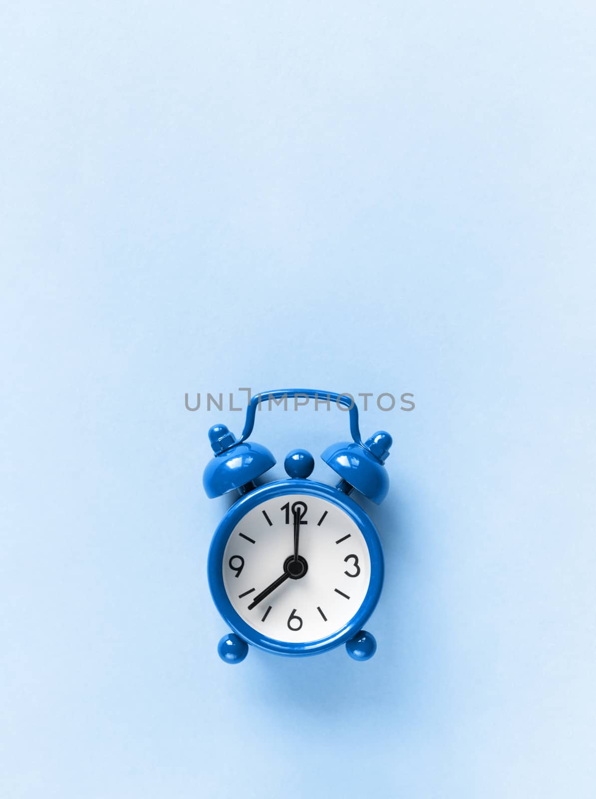 Small alarm clock on pastel background in Classic Blue colour, close-up, top view. Minimal retro style. Time management, Color of the year 2020 concept. Copy space for text. Vertical orientation.