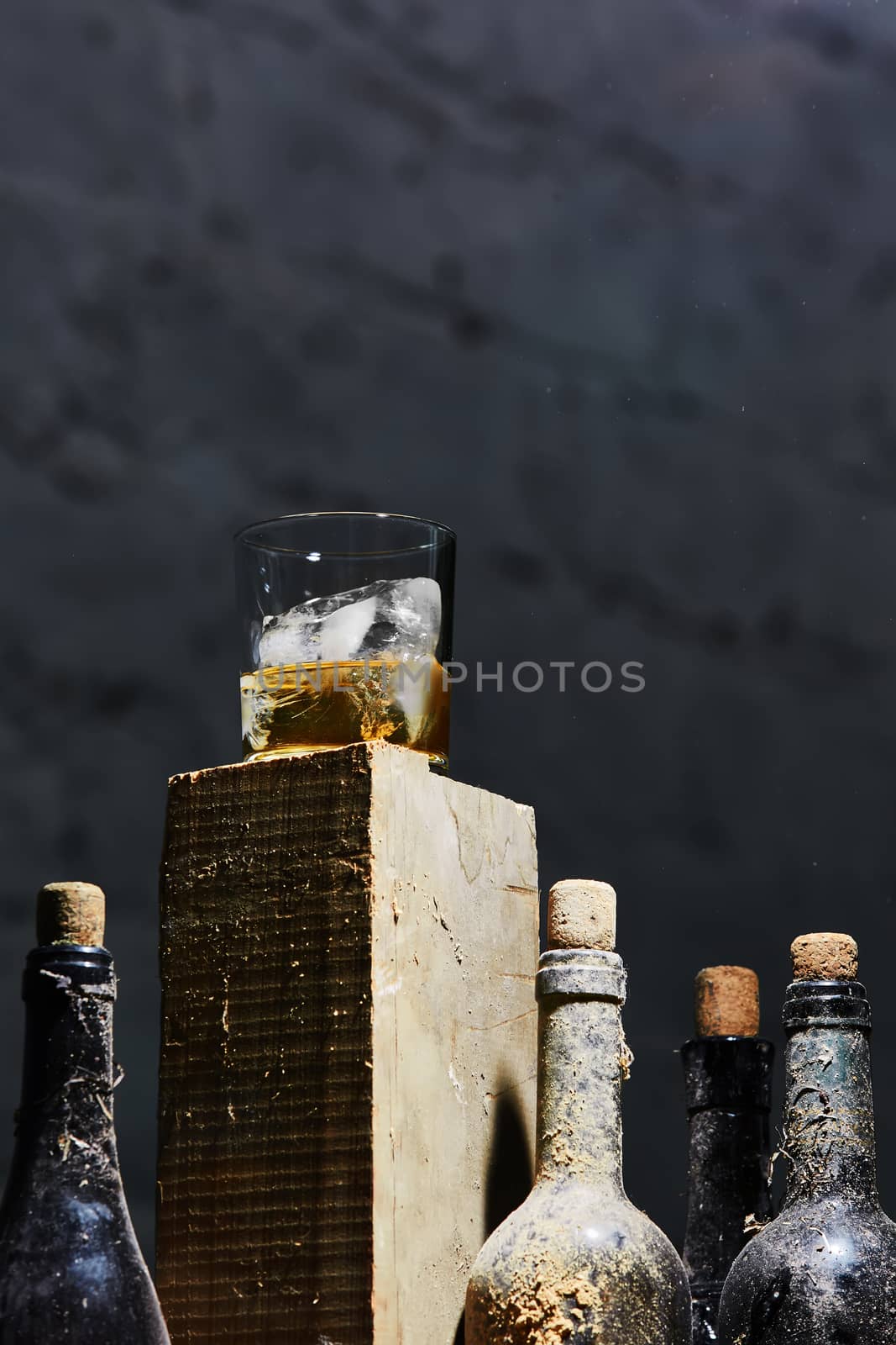 A glass of whiskey with ice on old wooden bar around the old bottles. Shallow dof