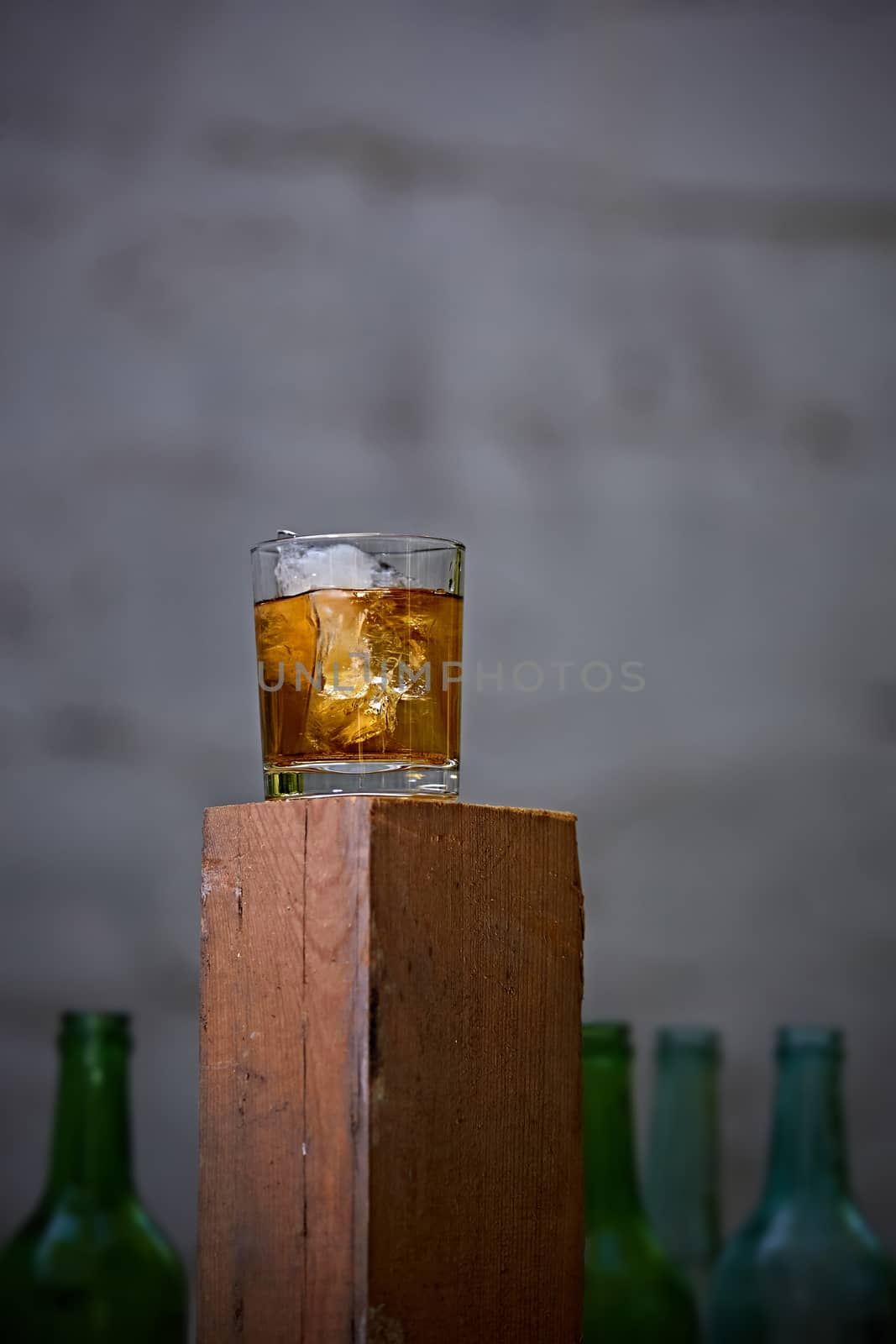 A glass of whiskey with ice on old wooden bar around the old bottles. Shallow dof