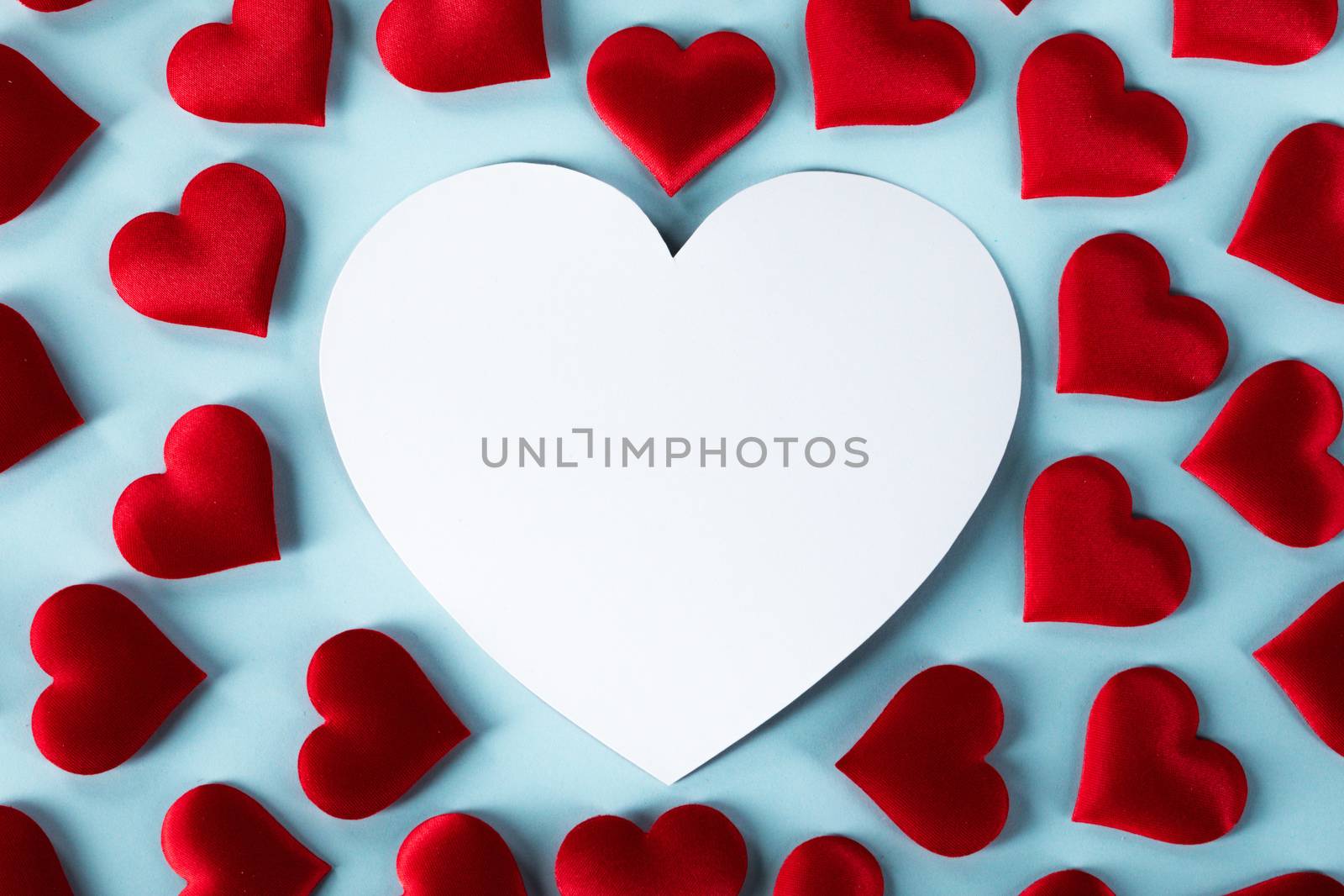 Valentine's day many red silk hearts and white heart shaped card on blue background, love concept