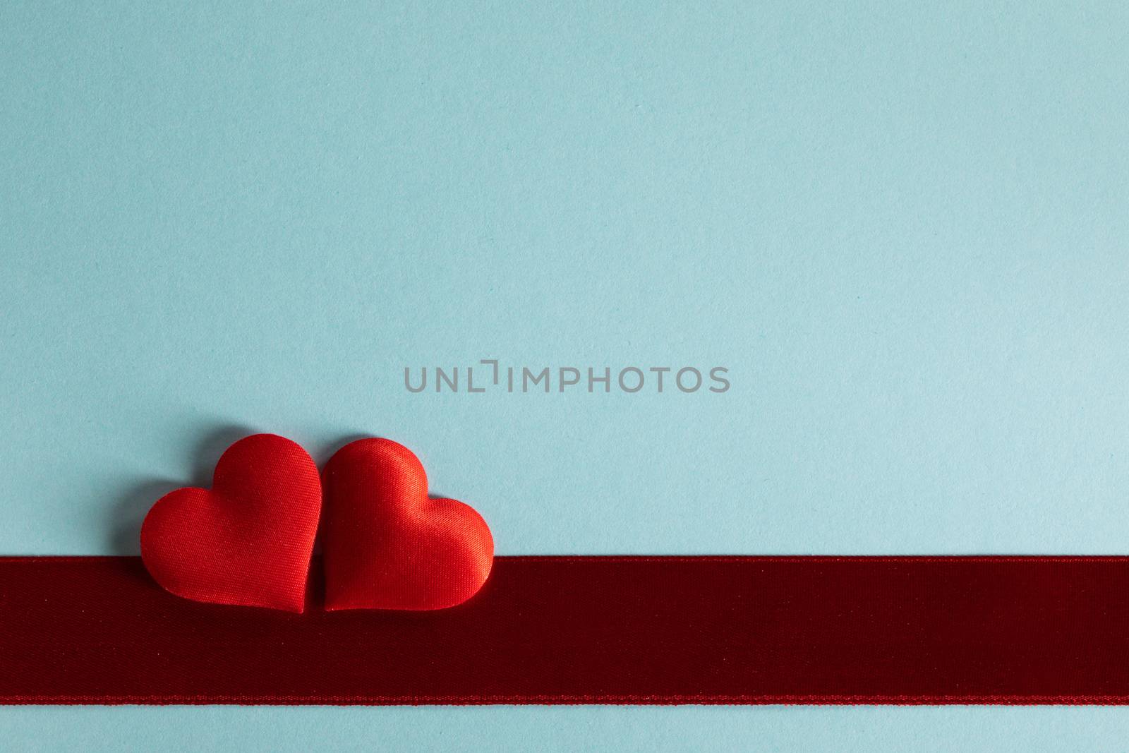 Valentine's day two red silk hearts and red satin ribbon on blue paper background, love concept