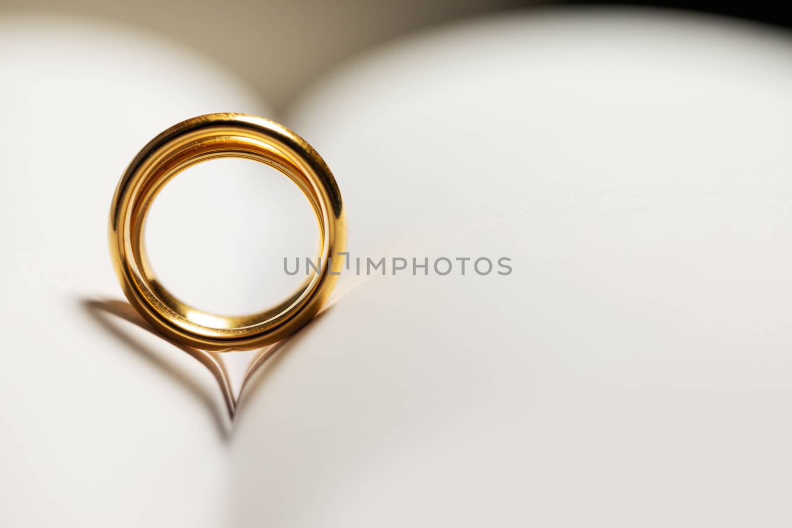 Two golden wedding rings on blank book pages background with copy space for text