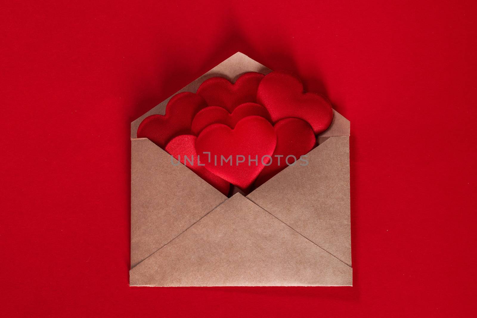 Valentine day love letter, envelope of craft paper with red hearts heap spread on white background.