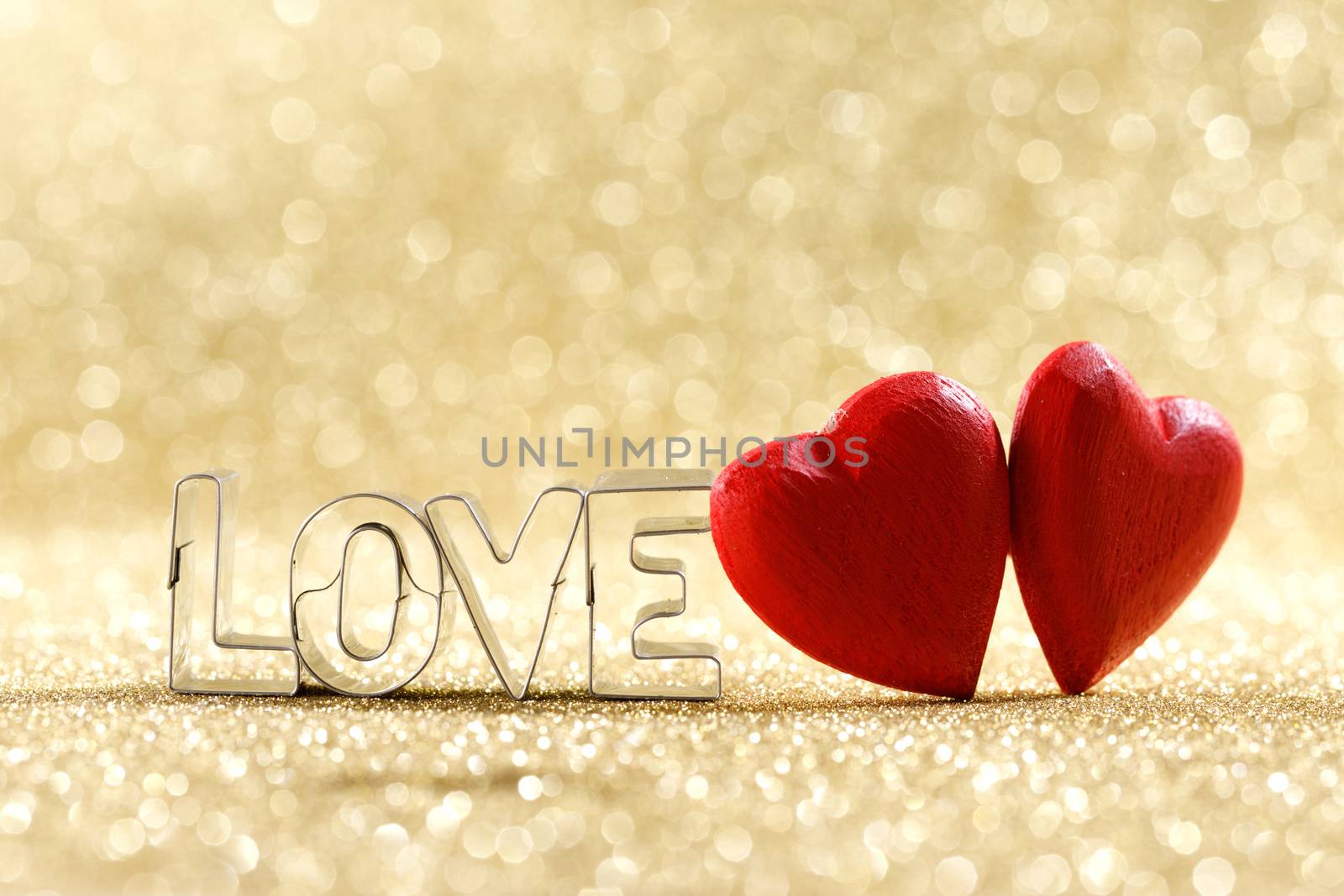 Two red handmade wooden hearts and word love on golden bright glitter lights bokeh background