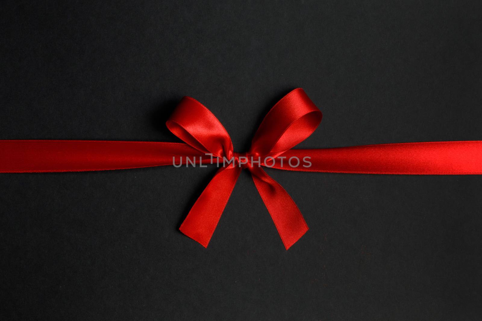 Red satin ribbon bow on black paper background