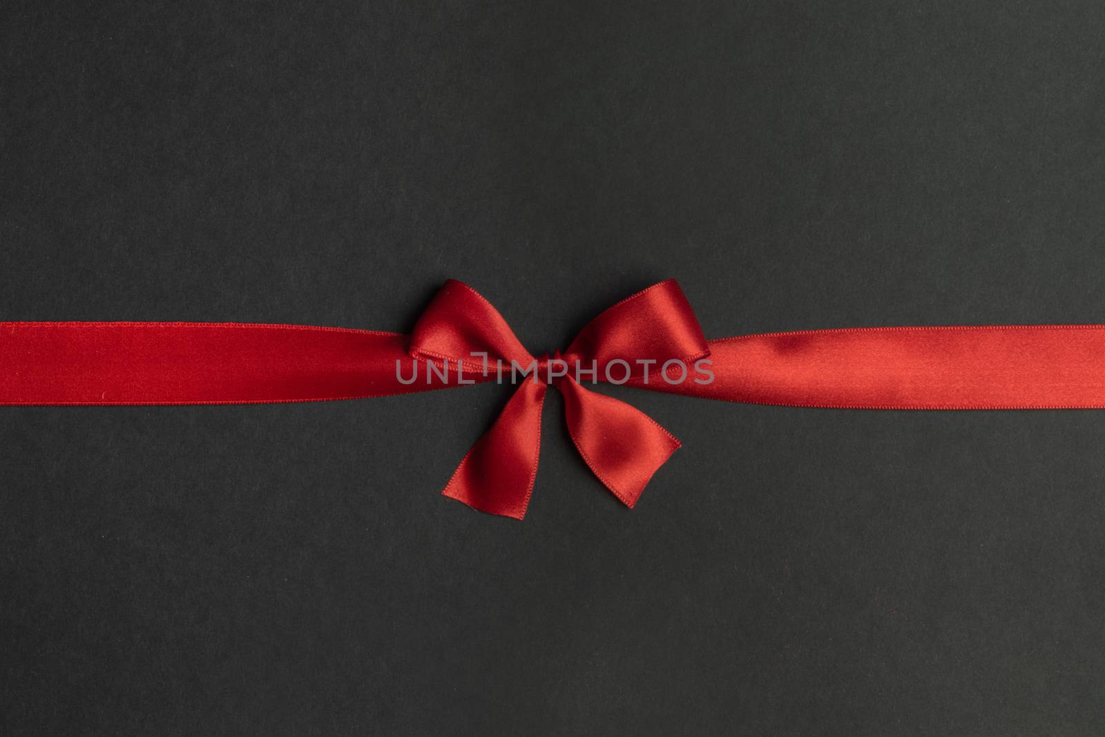 Red satin ribbon bow on black paper background