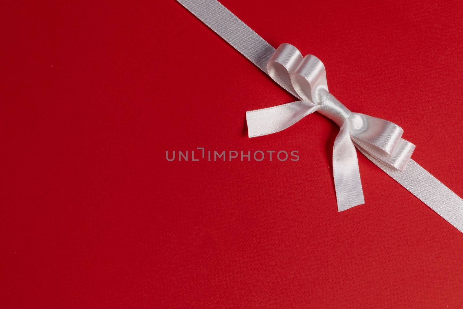 White satin ribbon bow on red paper background