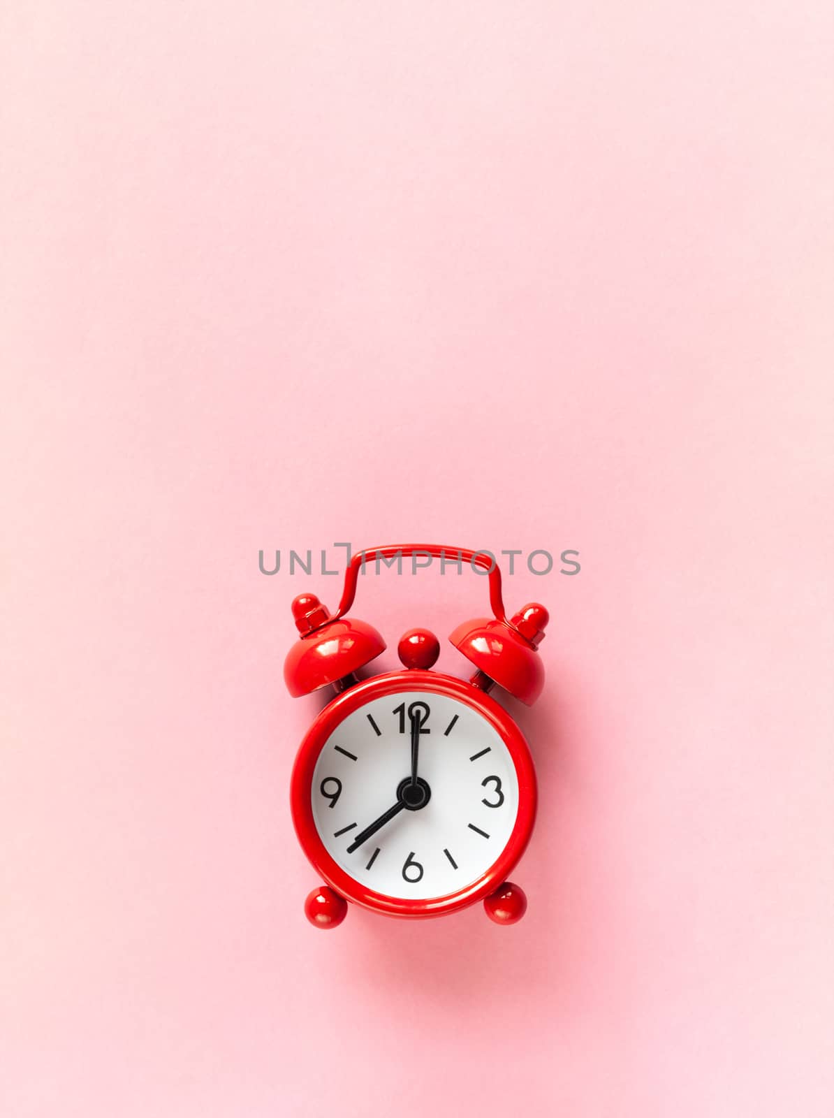 Red small alarm clock on pastel pink background with copy space, flat lay, macro. Minimalism style. Time management, countdown concept. Vertical orientation.